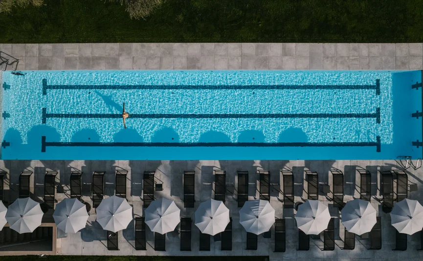 Aerial view of swimming pool with person in water and sun loungers with umbrellas