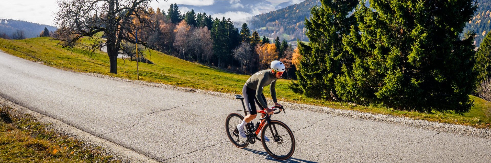 Cyclist rides on mountain road under sunny autumn sky with fog in valley
