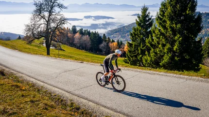 Cyclist rides on mountain road under sunny autumn sky with fog in valley