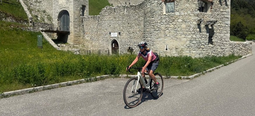 Cyclist riding past an ancient stone castle in a mountainous area