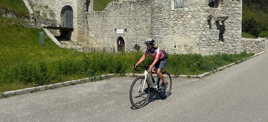 Cyclist riding past an ancient stone castle in a mountainous area