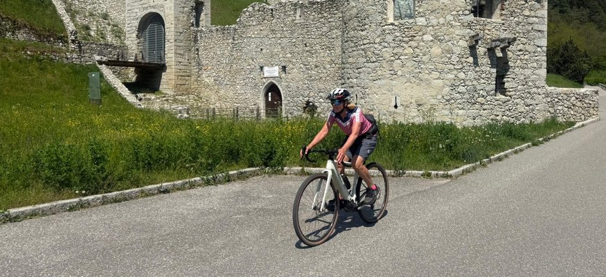 Radfahrer vor einer alten Steinburg in einer bergigen Landschaft