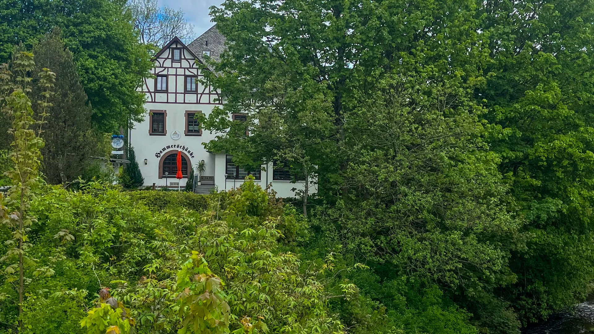 Haus hinter Bäumen an einem bewölkten Tag am Fluss