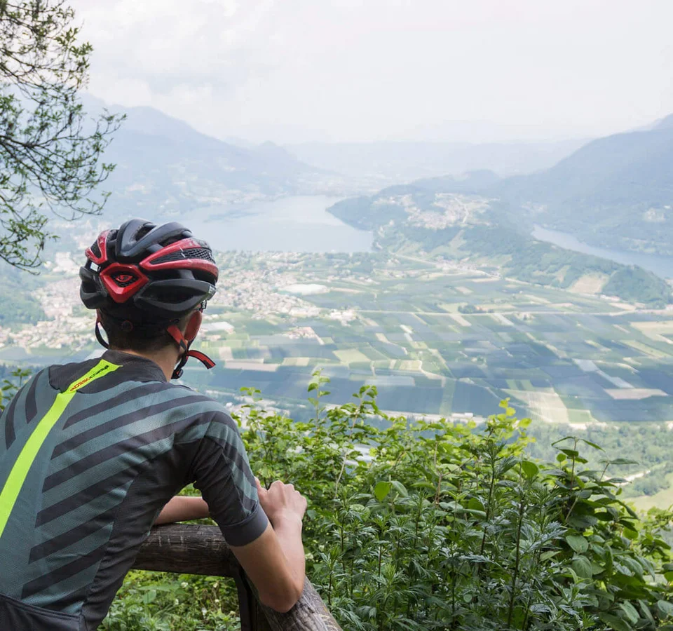 Zwei Radfahrer blicken von einem Berg auf ein Tal mit Fluss und Feldern