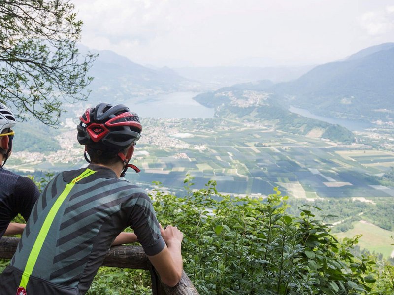 Zwei Radfahrer blicken von einem Berg auf ein Tal mit Fluss und Feldern