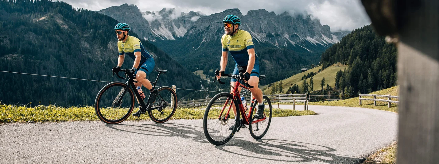 Graveln bis nach Bocconara zum Mittagessen © Jens Scheibe Zwei Radfahrer fahren bergauf auf einer kurvigen Straße mit Bergen im Hintergrund