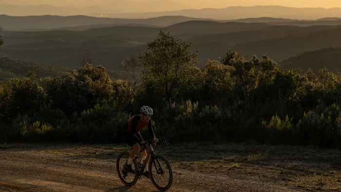 Gravelbiken in der Toskana © Tenuta il Cicalino Mountainbiker fährt auf Schotterweg bei Sonnenuntergang in hügeliger Landschaft