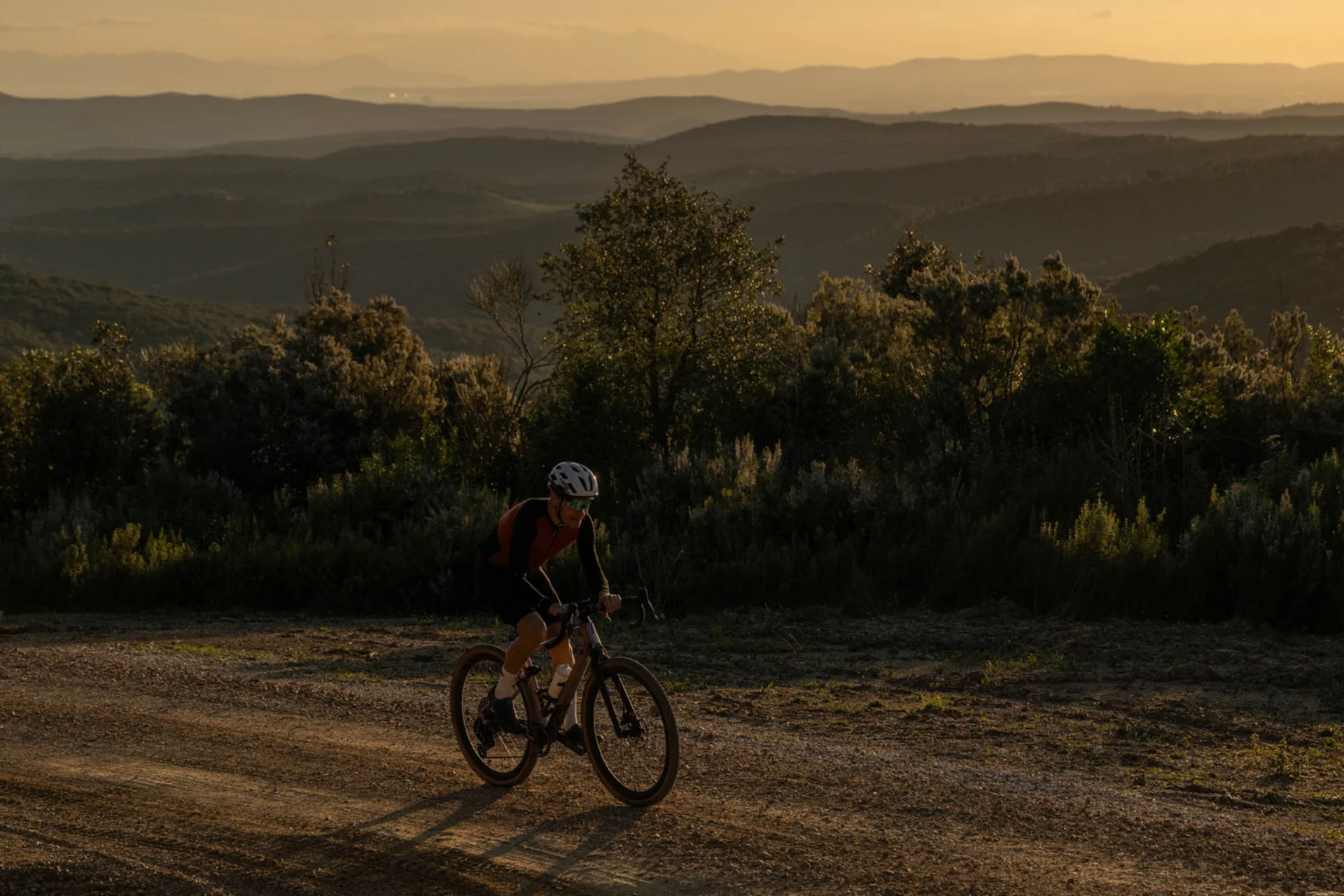 Gravelbike Holidays © Tenuta il Cicalino Mountainbiker fährt auf Schotterweg bei Sonnenuntergang in hügeliger Landschaft