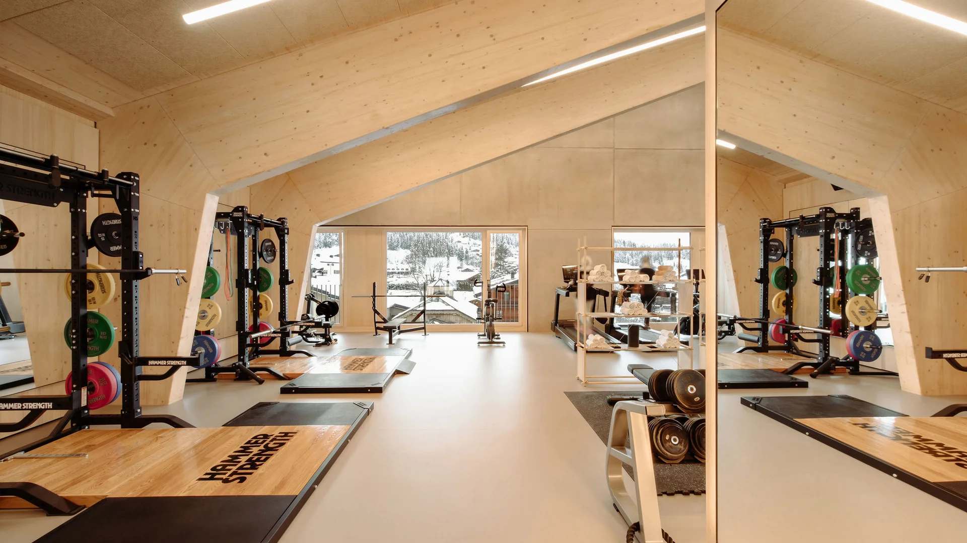Heller Fitnessraum mit Holzverkleidung und Gewichten vor Fenstern