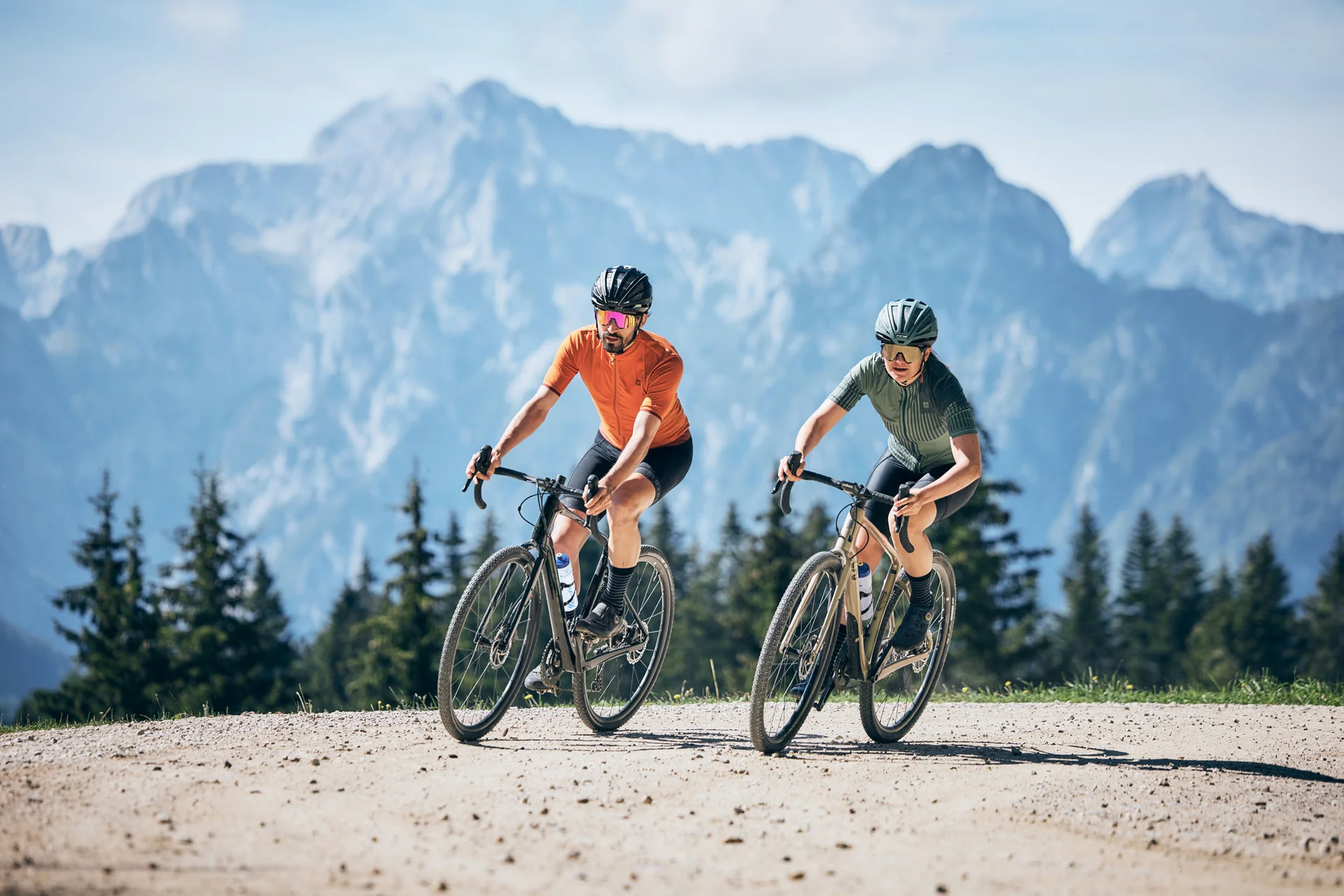 Zwei Radfahrer fahren auf Bergweg mit Bergpanorama im Hintergrund