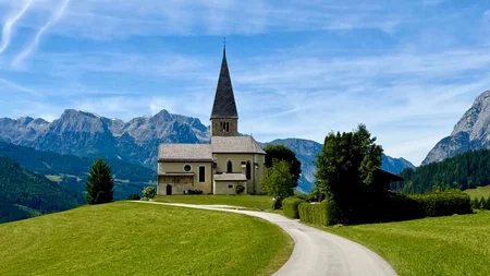 5 Gravel-Touren in der Salzburger Sportwelt, die du kennen solltest © Daniela Erner Kirche auf einem Hügel mit Bergkulisse und blauem Himmel