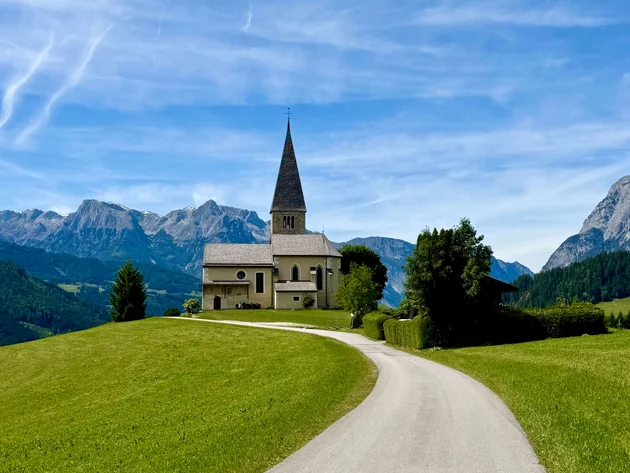 5 Gravel-Touren in der Salzburger Sportwelt, die du kennen solltest © Daniela Erner Kirche auf einem Hügel mit Bergkulisse und blauem Himmel