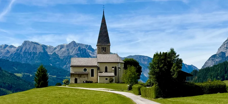 Kirche auf einem Hügel mit Bergkulisse und blauem Himmel