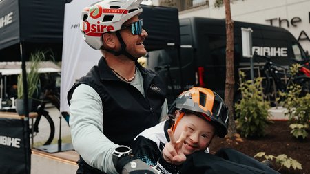 Mann mit Kind auf Mountainbike, Kind zeigt Friedenszeichen und lächelt