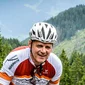 Man riding road bike on mountain road with pine trees in background