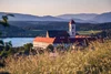Monastery with red roof by lake and mountains at sunset