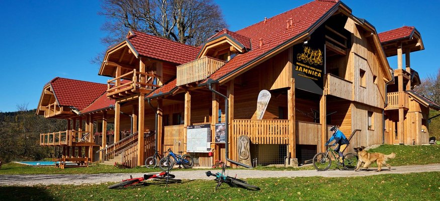 Holzhaus mit roten Dächern, Mountainbikes und Person mit Hund im Garten