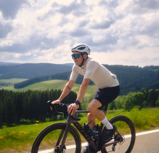 Radfahrer in Sportkleidung fährt auf Landstraße mit grüner Landschaft im Hintergrund