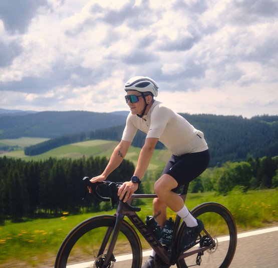 Gravelbike Urlaub im Schwarzwald © David Lemanski Radfahrer in Sportkleidung fährt auf Landstraße mit grüner Landschaft im Hintergrund