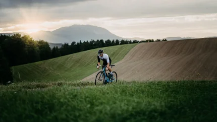 Cyclist rides on rural road at sunset with hills and cloudy sky