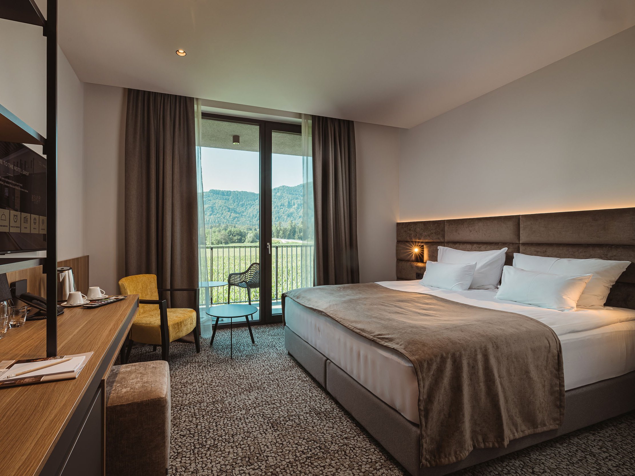 Modernes Hotelzimmer mit Doppelbett, Schreibtisch und Balkon mit Aussicht auf Berge