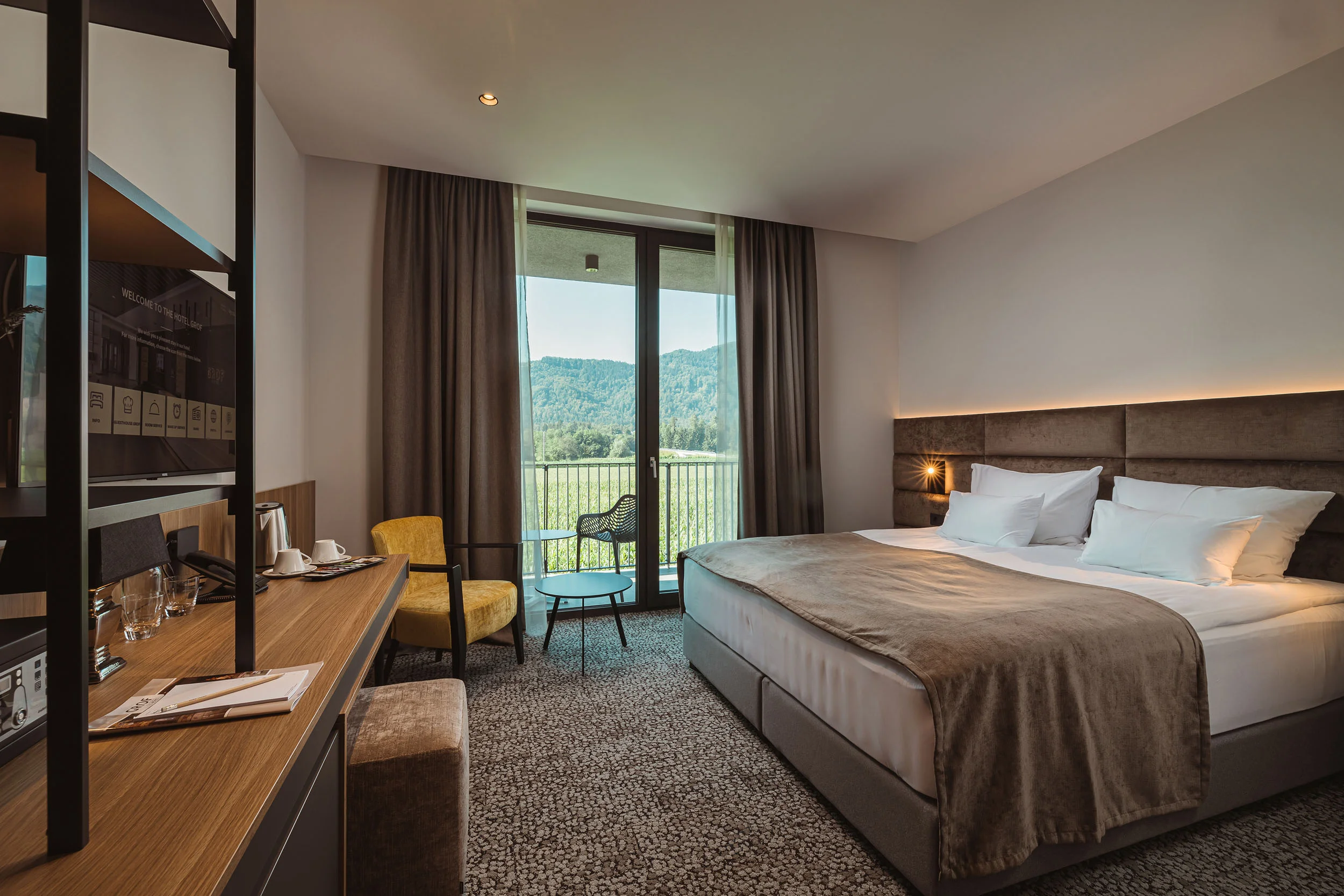 Modern hotel room with double bed, desk, and balcony overlooking mountains