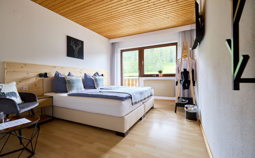 Helles Hotelzimmer mit Doppelbett, Holzbalkendecke und großem Fenster