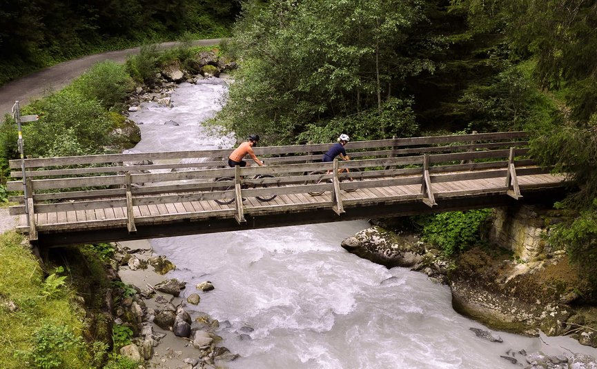 Zwei Radfahrer fahren über eine Holzbrücke über einen Fluss in einem Wald