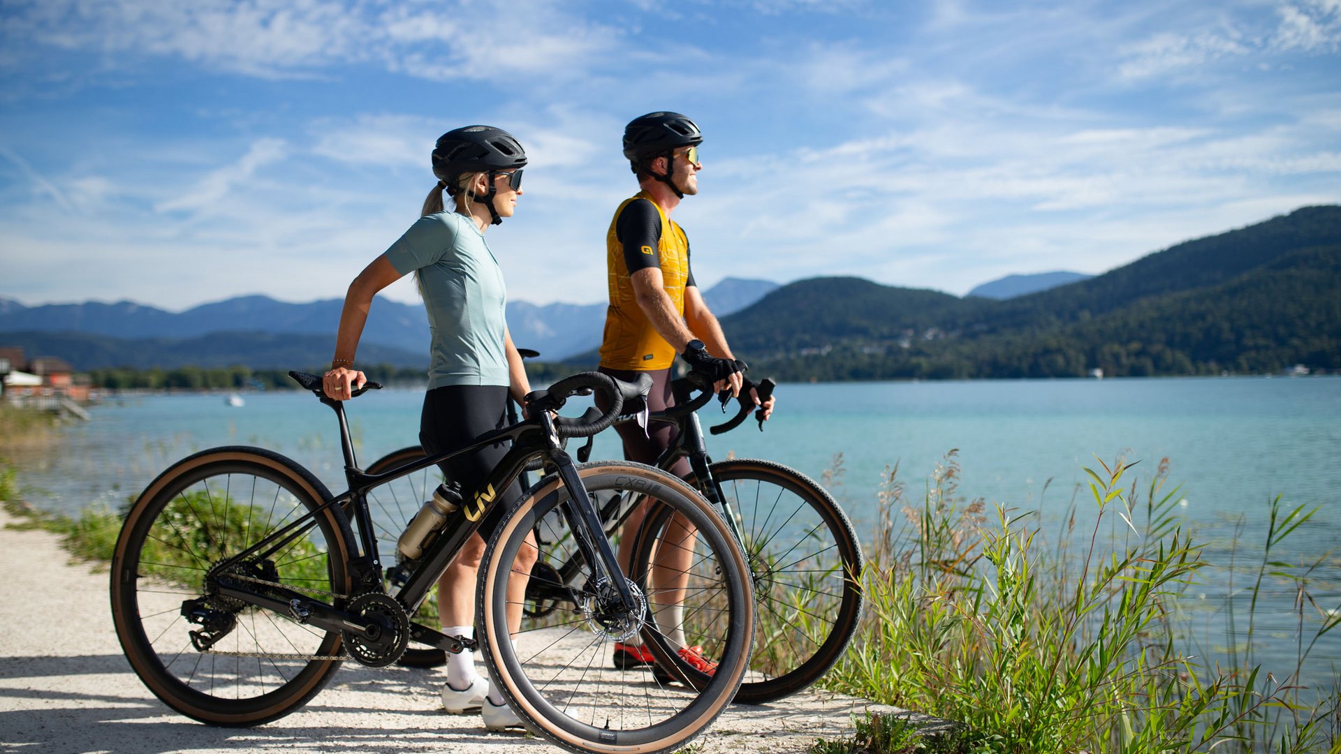 Zwei Radfahrer stehen mit ihren Fahrrädern an einem See mit Bergblick