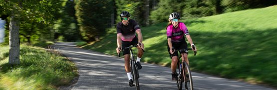 Zwei Radfahrer auf einer bewaldeten Landstraße unterwegs