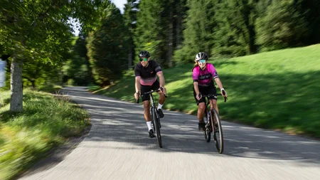 Zwei Radfahrer auf einer bewaldeten Landstraße unterwegs