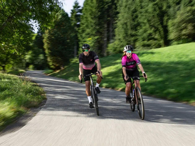 Zwei Radfahrer auf einer bewaldeten Landstraße unterwegs