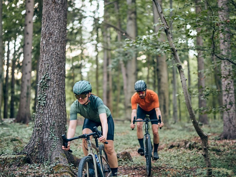 Zwei Radfahrer fahren durch einen Wald auf einem schmalen Pfad