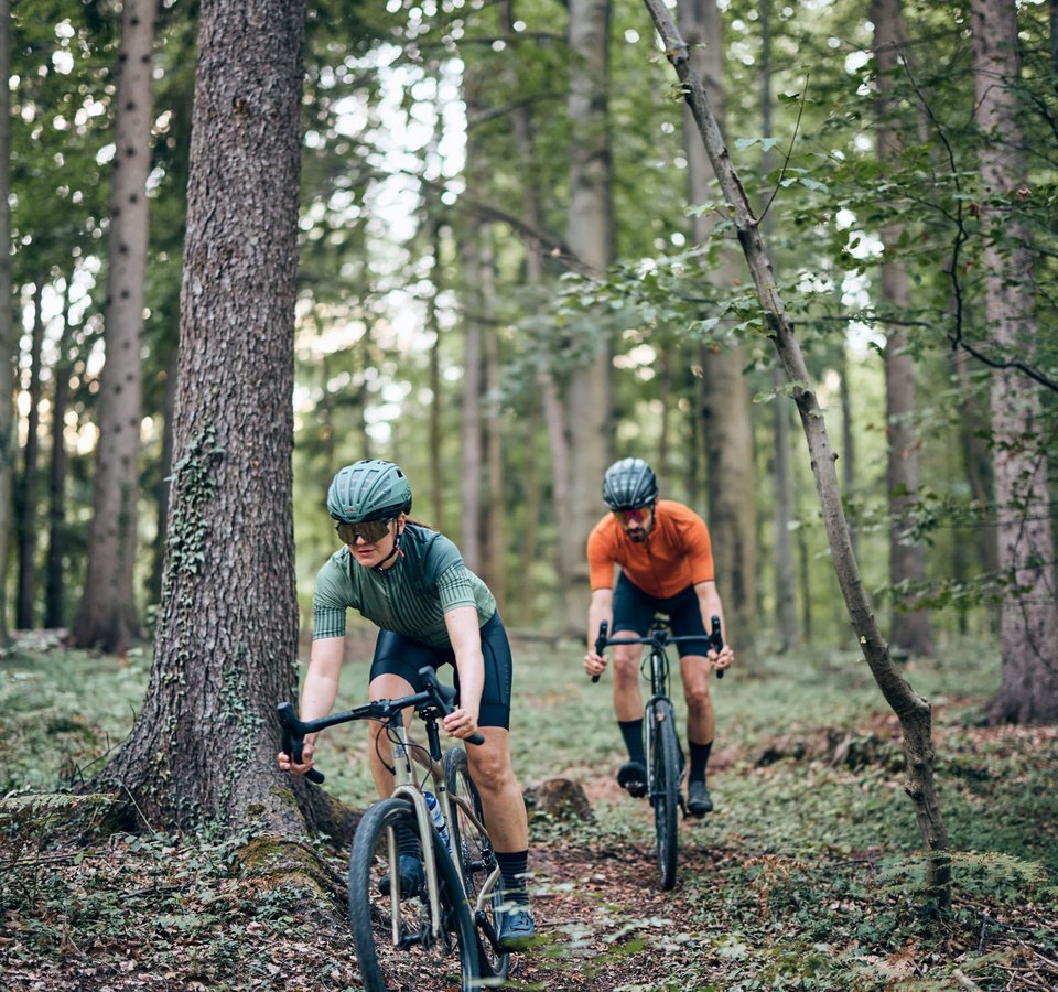 Zwei Radfahrer fahren durch einen Wald auf einem schmalen Pfad