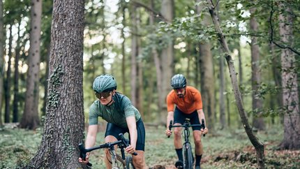 Zwei Radfahrer fahren durch einen Wald auf einem schmalen Pfad