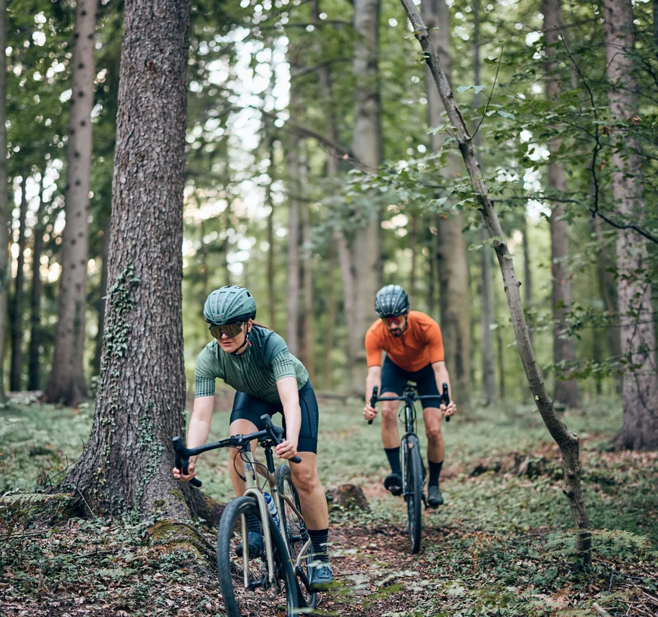 Zwei Radfahrer fahren durch einen Wald auf einem schmalen Pfad