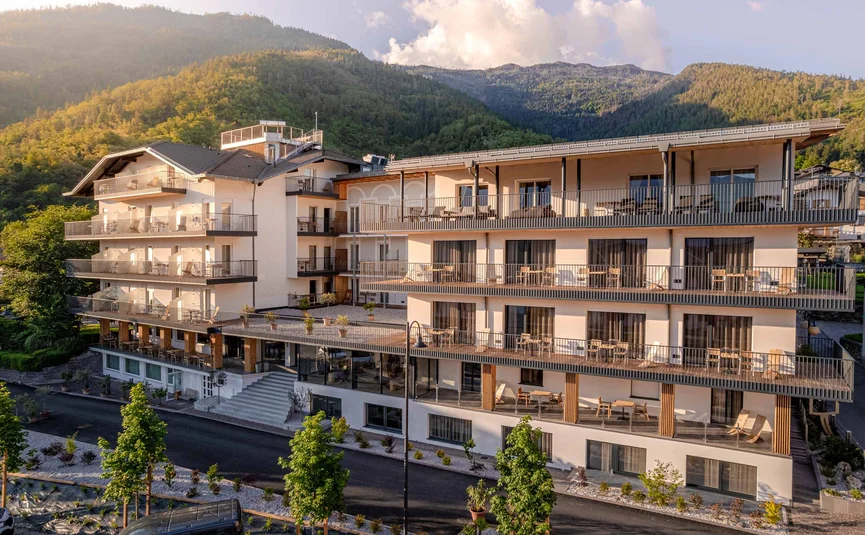 Cristallo Sport & Wellness Hotel **** © Andrea Acler Modern hotel building with balconies in sunlight and forested mountains