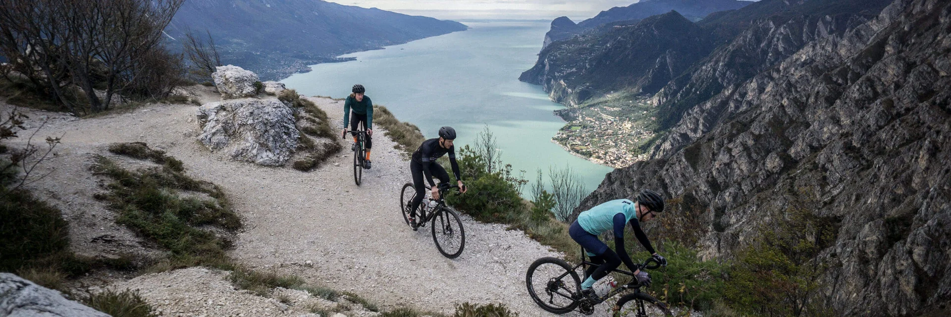 Three cyclists on a mountain trail overlooking a lake and mountains