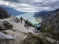Three cyclists on a mountain trail overlooking a lake and mountains