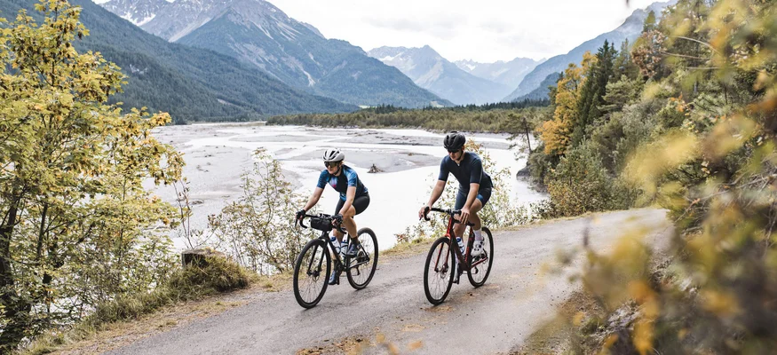 Werde zum GravelKING in Gravel.Tirol © Andreas Vigl Zwei Radfahrer fahren entlang eines Bergwegs neben einem Fluss
