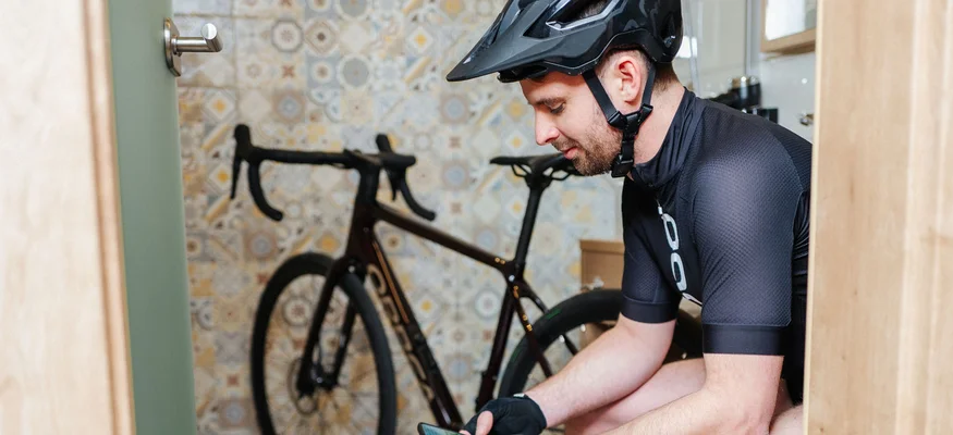 Radfahrer mit Helm überprüft Smartphone in einem Raum mit Fahrrad