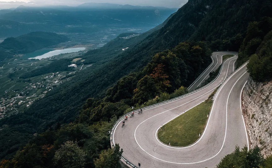 Fahrradfahrer auf Serpentinenstraße in bewaldeten Bergen mit Tal und See im Hintergrund