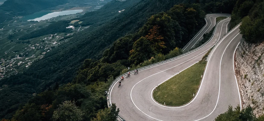 Fahrradfahrer auf Serpentinenstraße in bewaldeten Bergen mit Tal und See im Hintergrund