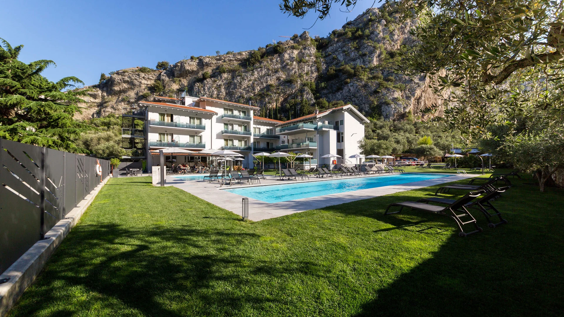 Hotel mit Swimmingpool und Liegestühlen vor felsigem Berg