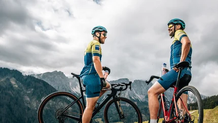 Two cyclists with mountain bikes standing on a mountain trail under cloudy sky
