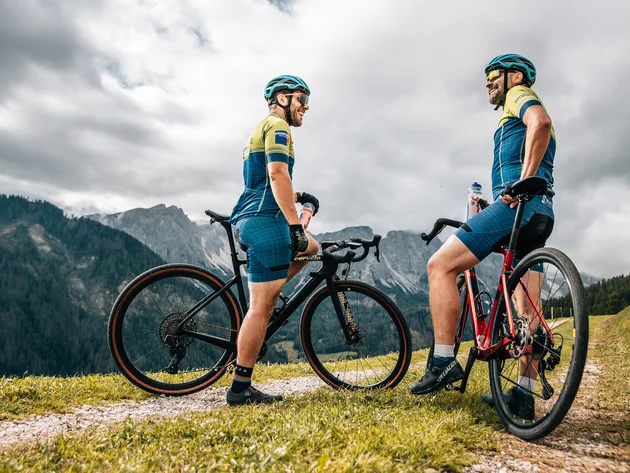 Zwei Radfahrer mit Mountainbikes stehen auf einem Bergweg vor bewölktem Himmel