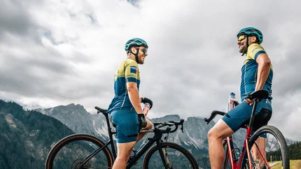 Zwei Radfahrer mit Mountainbikes stehen auf einem Bergweg vor bewölktem Himmel