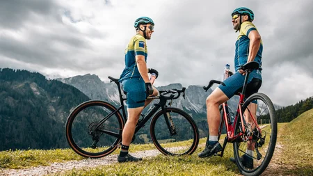 Zwei Radfahrer mit Mountainbikes stehen auf einem Bergweg vor bewölktem Himmel