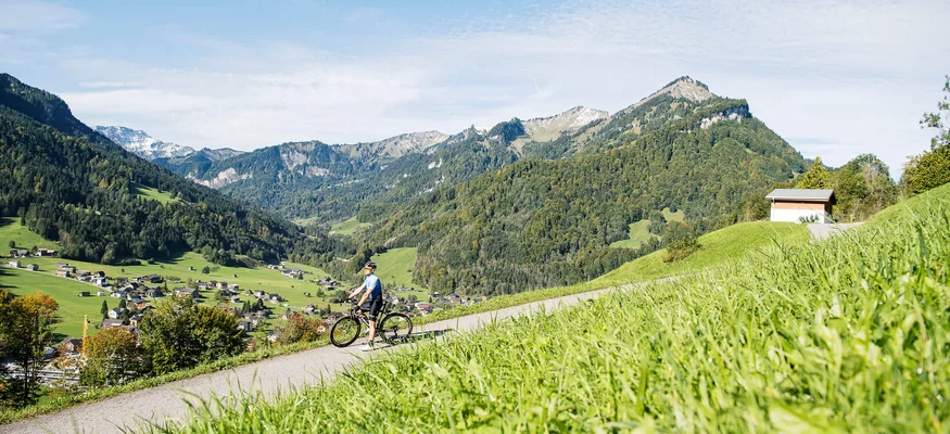 Müde Beine, volle Bäuche, offene Herzen © Alex Kaiser Radfahrer auf einem Hügel mit Blick auf ein Tal und Berge bei Sonnenschein