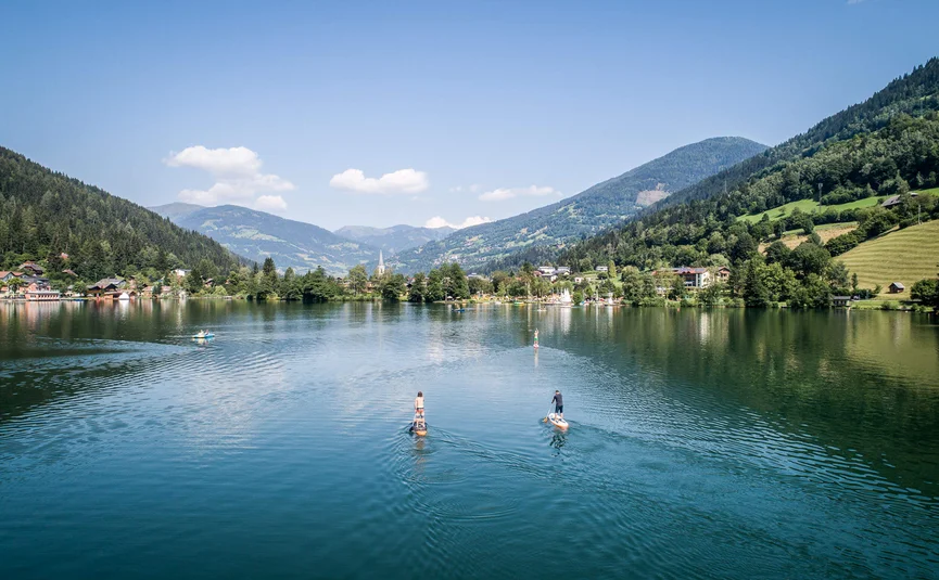 Two people paddleboarding on a mountain lake under clear sky